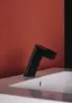 Schwarze Waschtischarmatur von Ideal Standard, in schräger Position über einem weißen Waschbecken, vor einer rot gestrichenen Wand platziert.